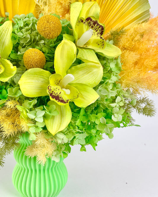 Bouquet of yellow and green preserved flowers in a green vase on a white background