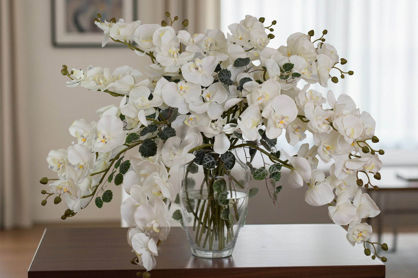 White orchid arrangement in a clear vase on a wooden table with a blurred indoor background
