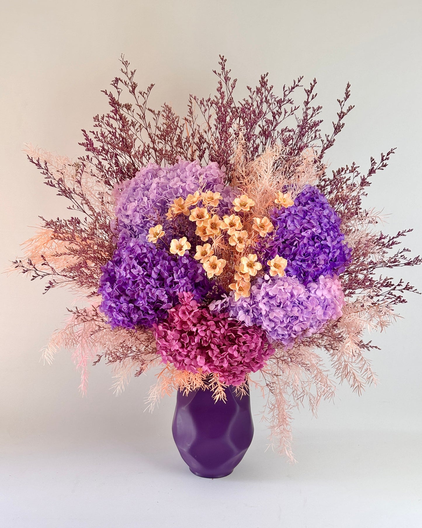 Bouquet of dried flowers in a purple vase on a light background
