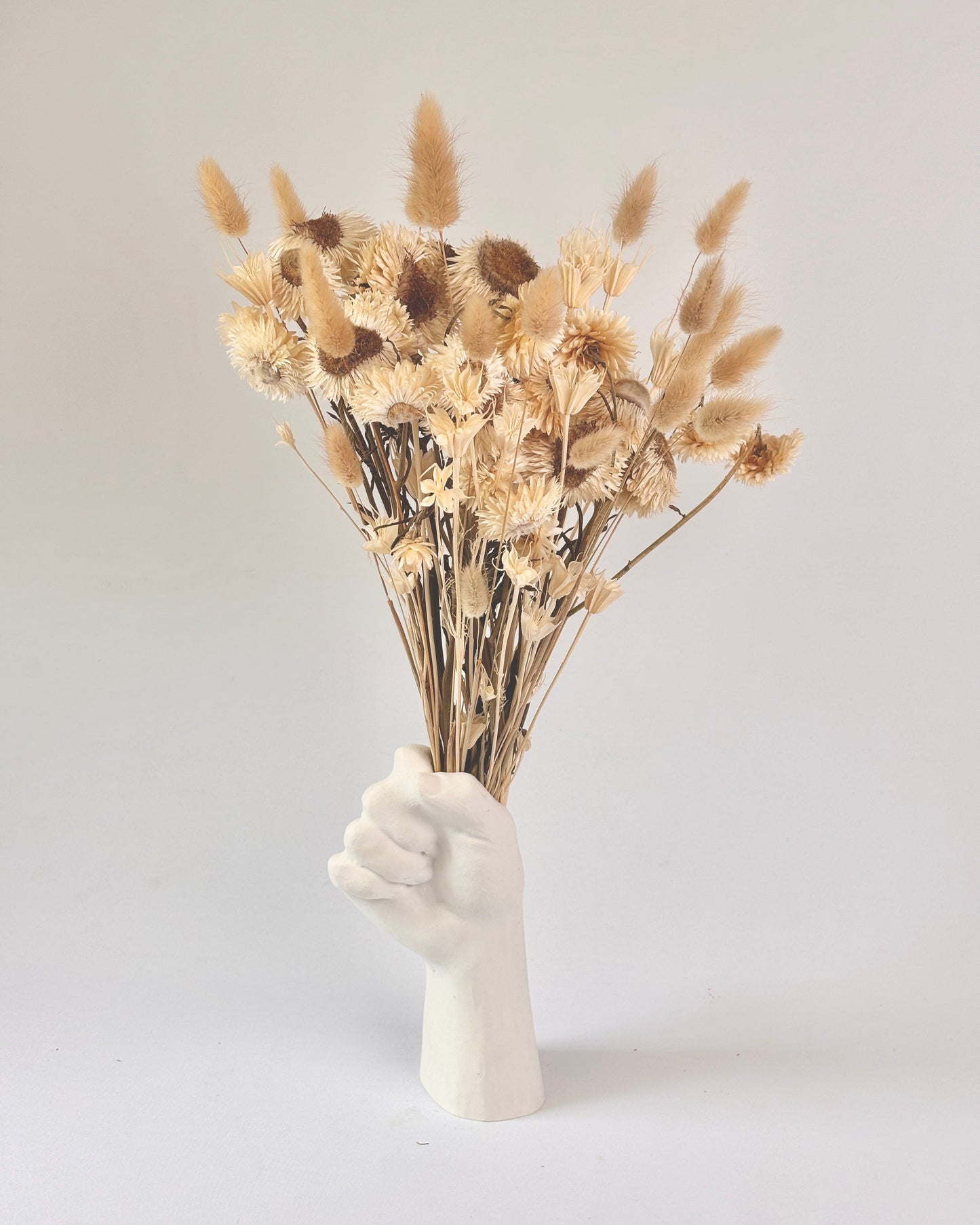 White hand-shaped vase holding dried flowers on a light gray background
