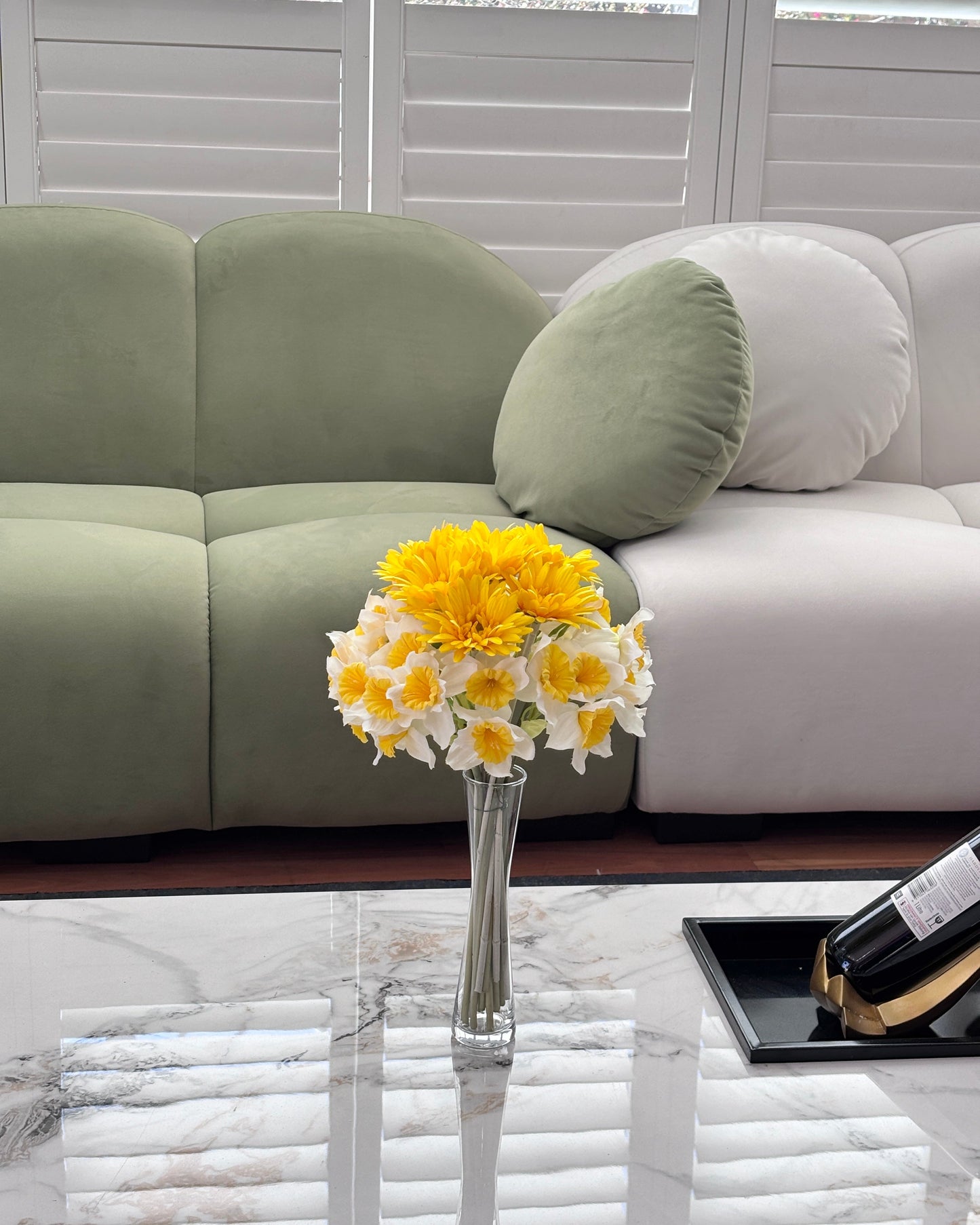 Modern living room with a gray sofa, a vase of yellow and white flowers, and a bottle on a coffee table.