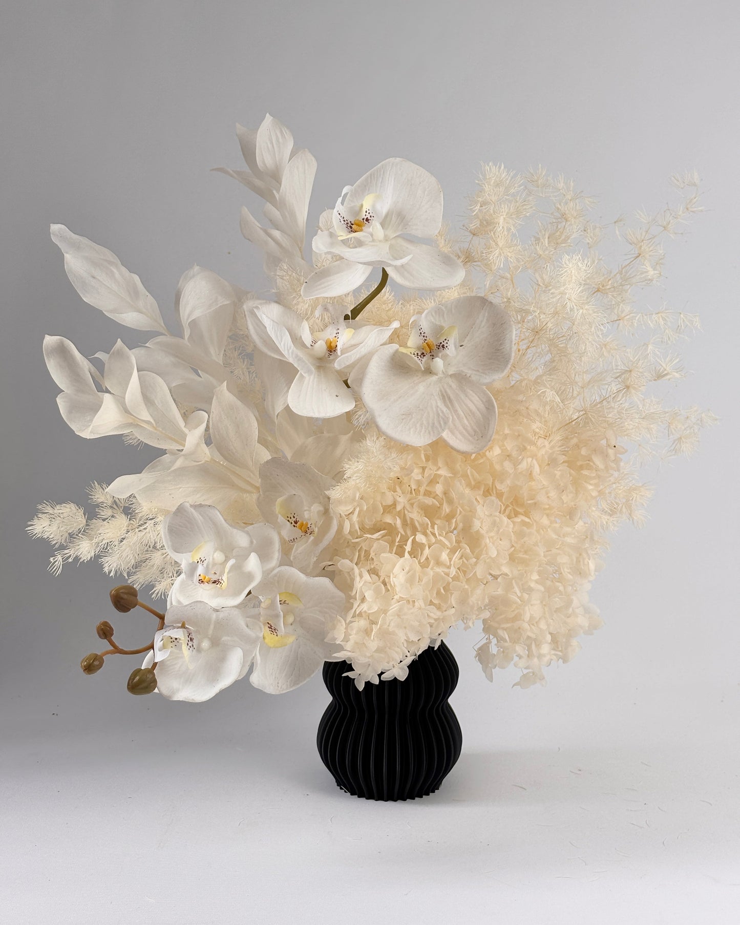 Bouquet of orchid flowers and white dried flowers in a black vase on a gray background