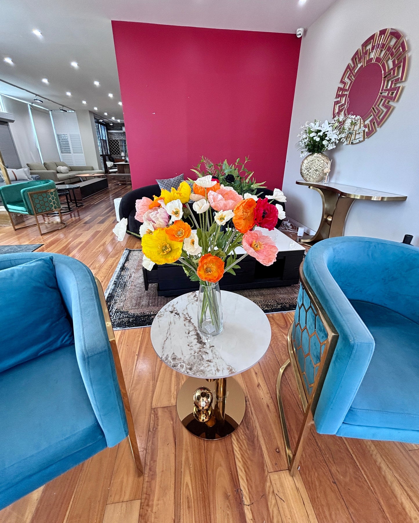 Modern living room with blue chairs, a round table with flowers, and a pink accent wall.