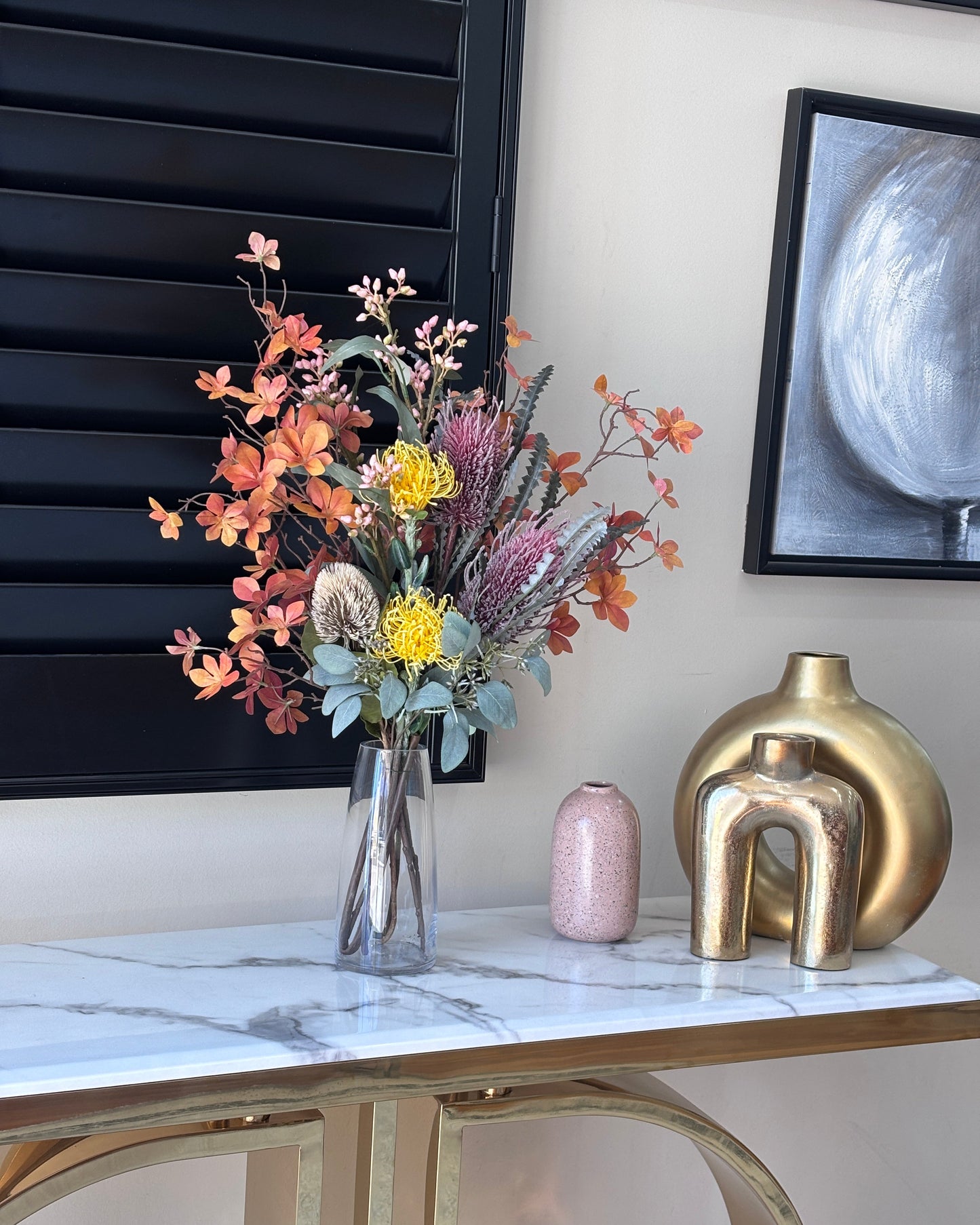 Decorative flowers on a black surface with a gold abstract sculpture and marble wall in the background.