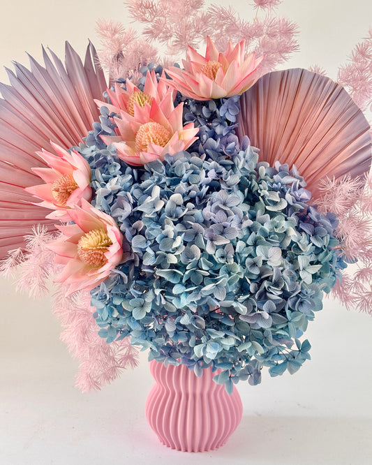 Bouquet preserved pink and blue flowers in a pink vase with pink feathers on a white background