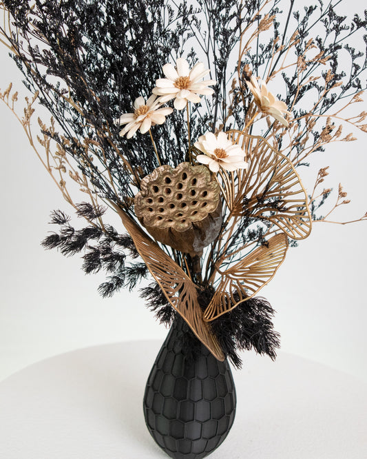 Decorative arrangement of dried flowers and leaves in a black vase