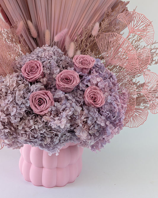 Pink and purple floral arrangement in a pink textured vase against a light background.