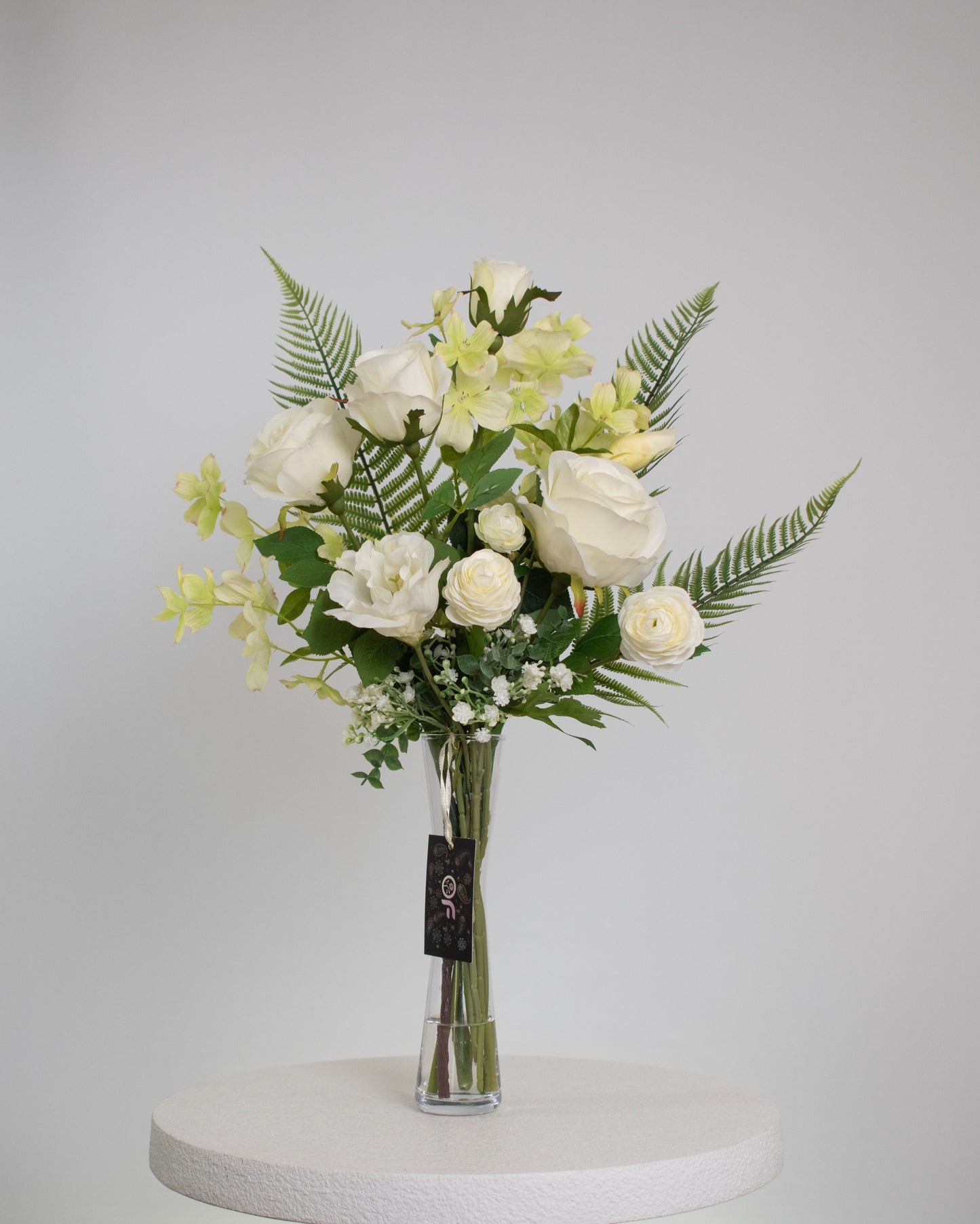 Artificial white floral arrangement with roses, delicate blooms, and ferns in a tall clear glass vase with acrylic water
