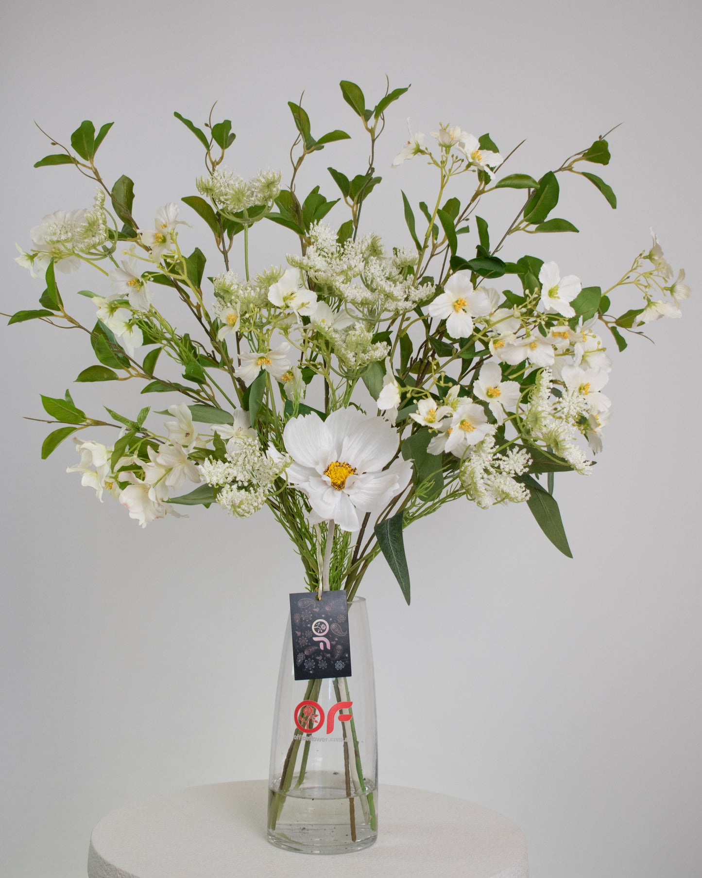 Artificial white floral arrangement with lush greenery, arranged in a clear glass vase with acrylic water