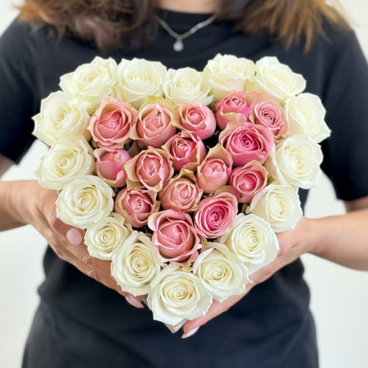 Heart-shaped bouquet of pink and white roses held by a person against a plain background