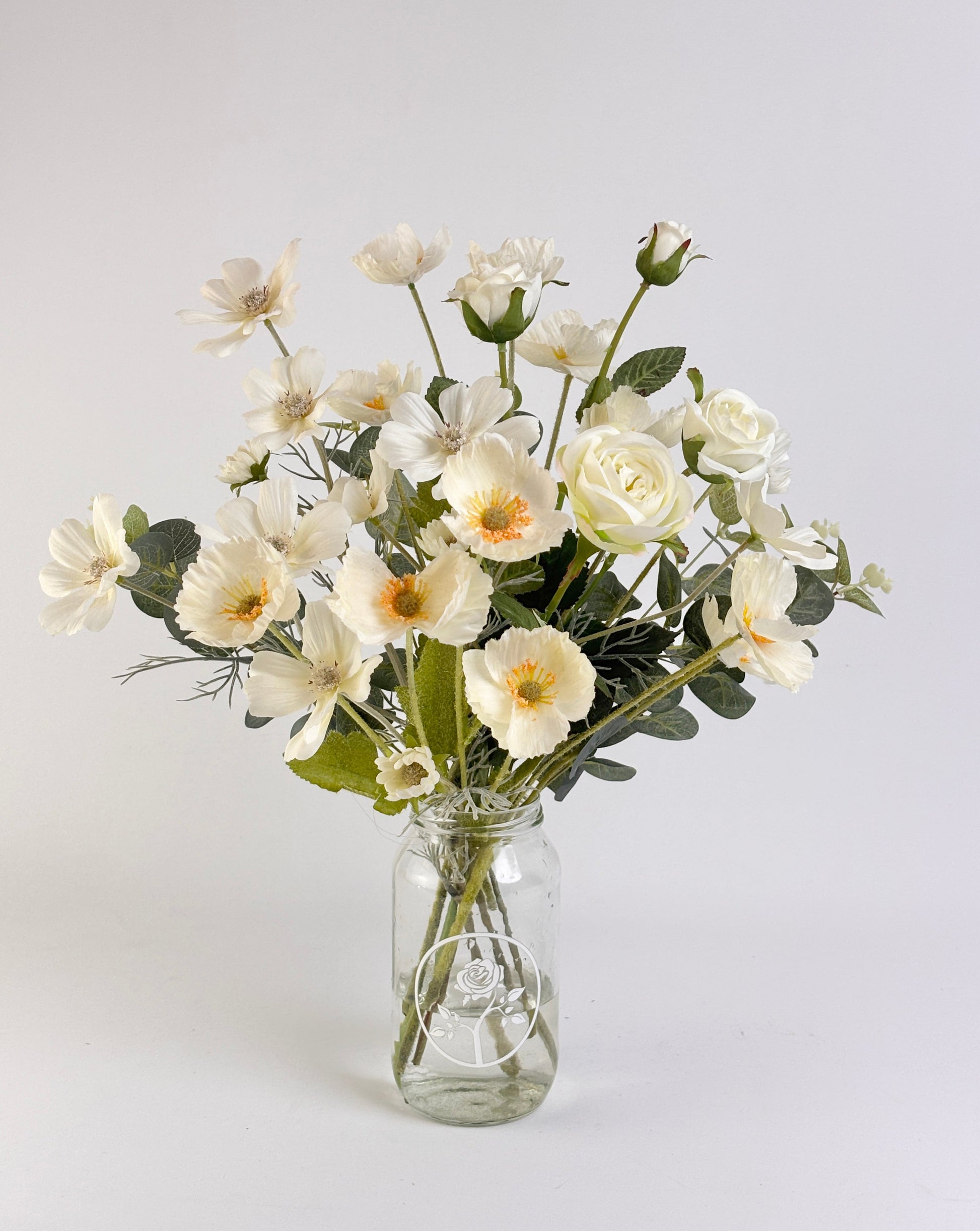 Bouquet of white silk flowers in a clear glass vase on a light gray background