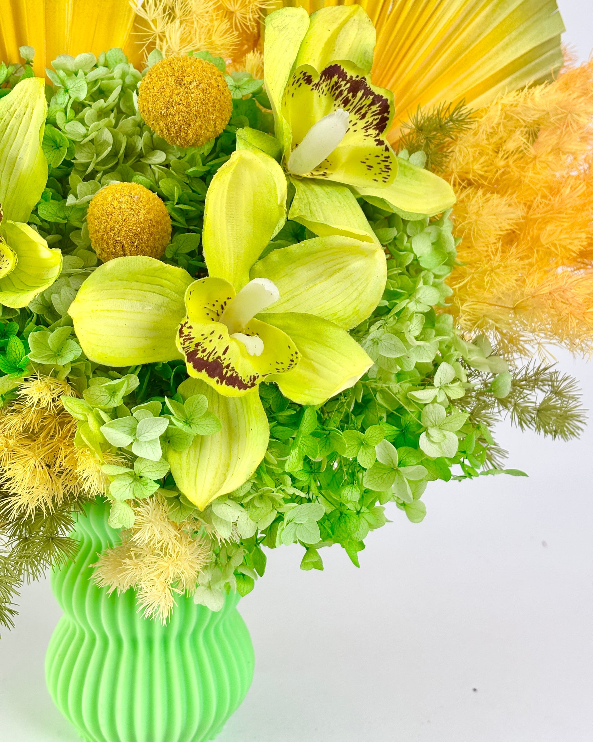 Bouquet of yellow and green preserved flowers in a green vase on a white background