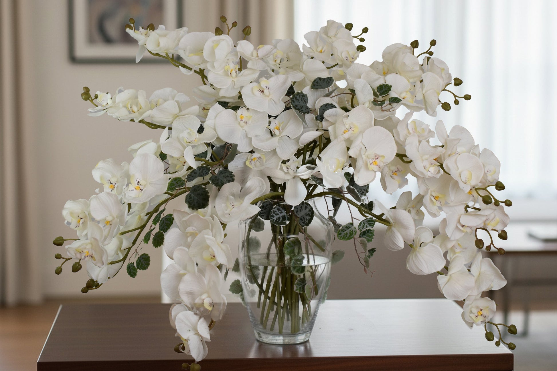 White orchid arrangement in a clear vase on a wooden table with a blurred indoor background