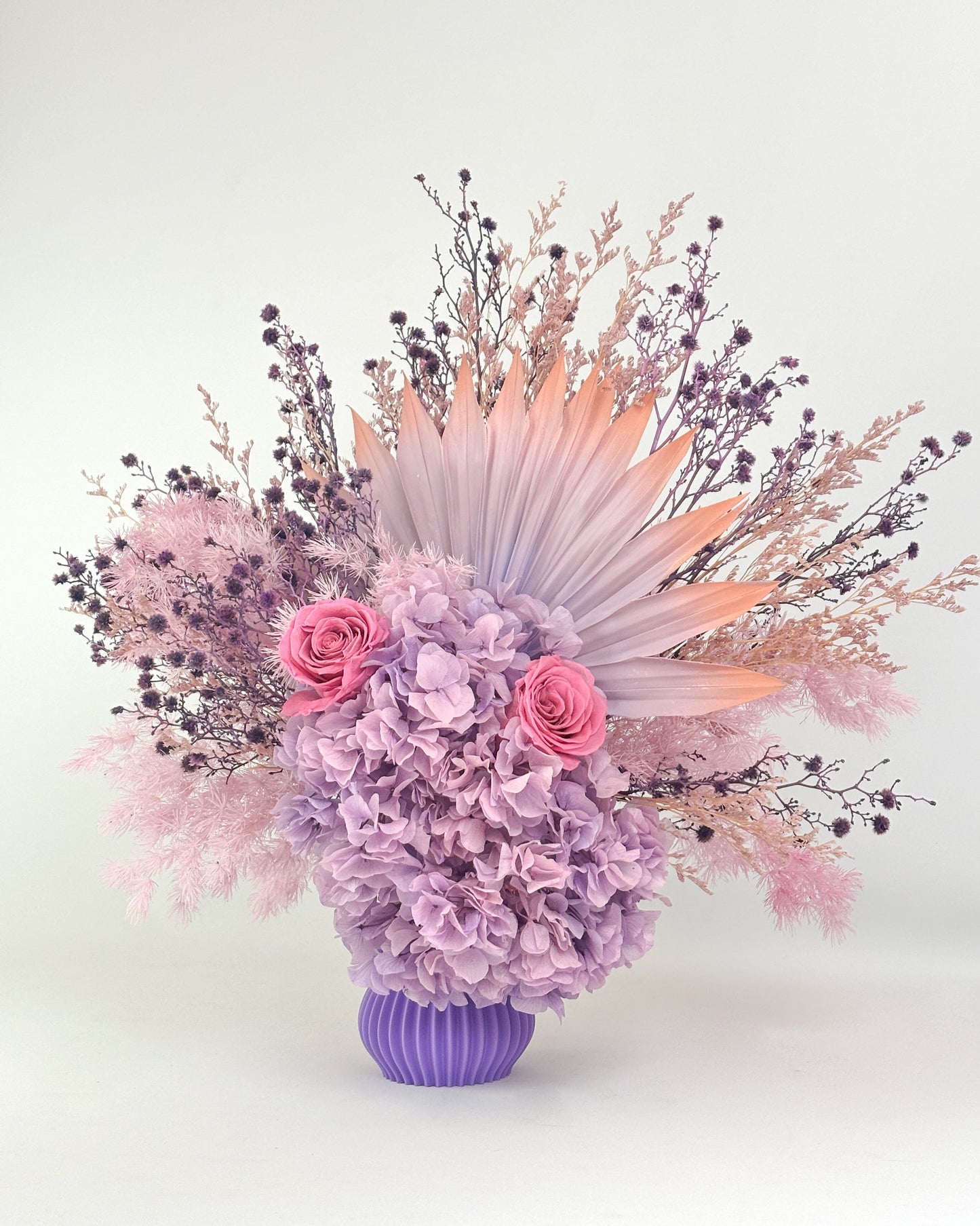 Dried Floral arrangement with lilac purple flowers in a purple vase on a white background