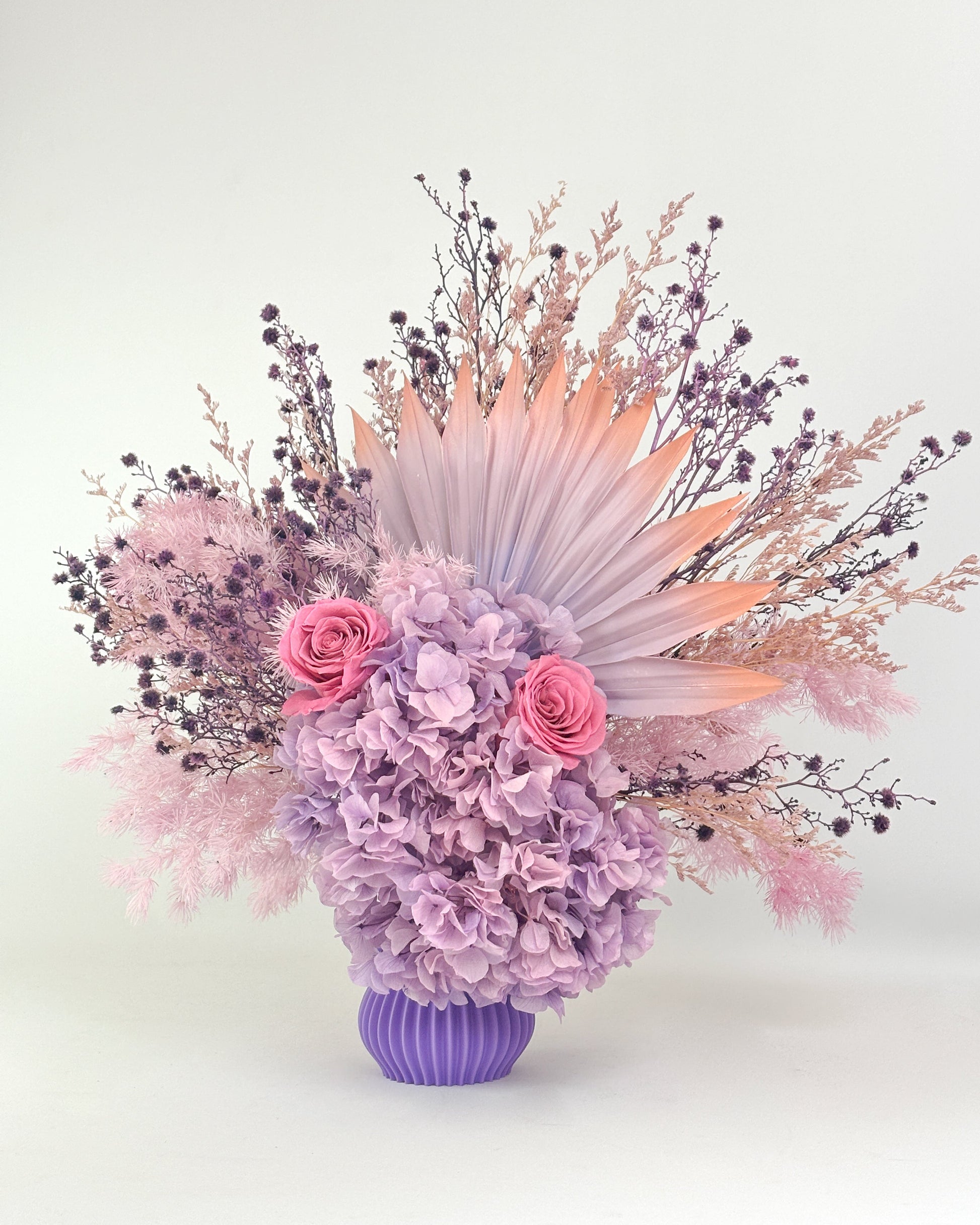 Dried Floral arrangement with lilac purple flowers in a purple vase on a white background