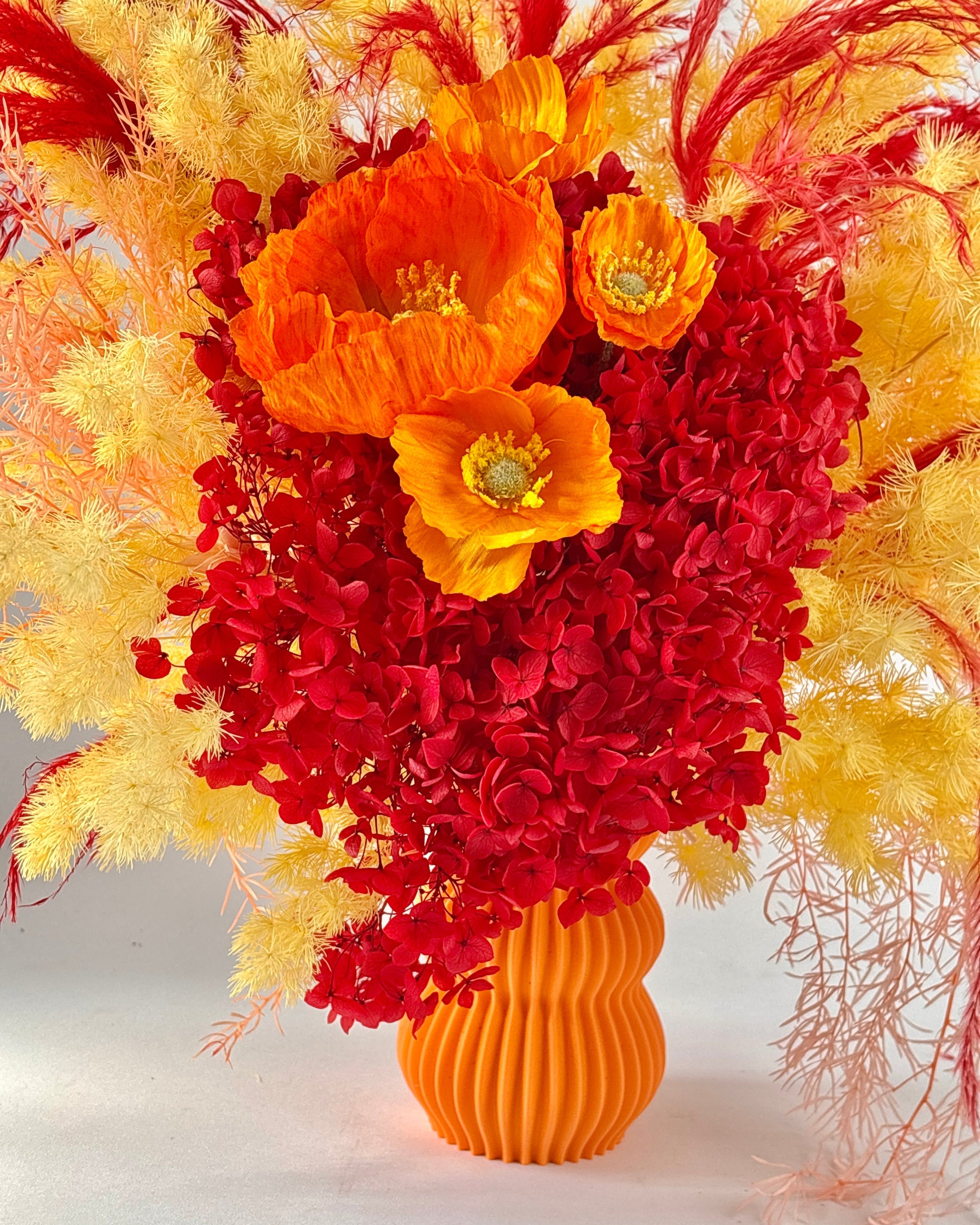 Bouquet of red and orange flowers in an orange vase on a white background