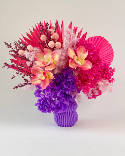 Colorful preserved floral arrangement with a purple vase on a white background