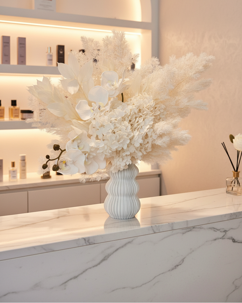 Decorative white dried floral arrangement in a white vase on a marble surface with a blurred background