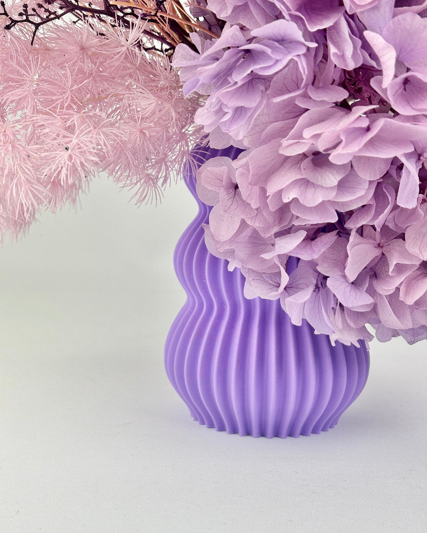 Purple ribbed vase with pink and purple flowers on a light gray background