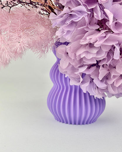 Purple ribbed vase with pink and purple flowers on a light gray background
