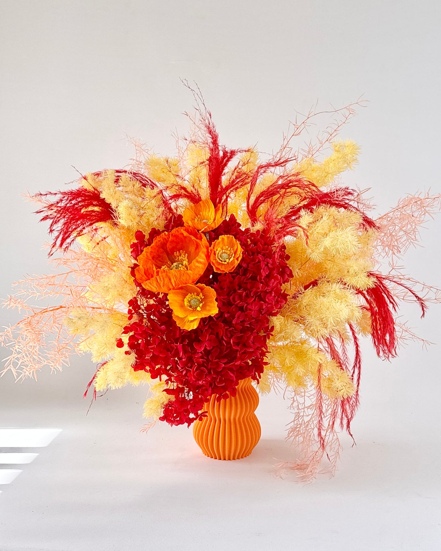 Bouquet of red and yellow dried flowers in an orange vase on a white background,