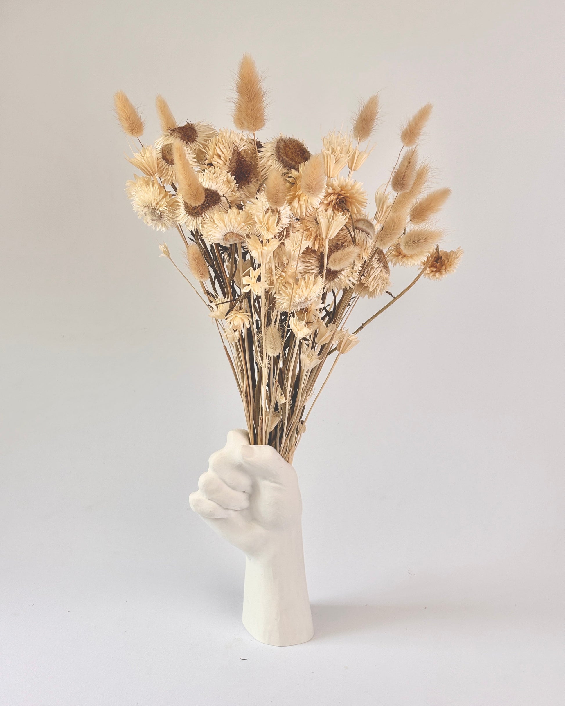 White hand-shaped vase holding dried flowers on a light gray background