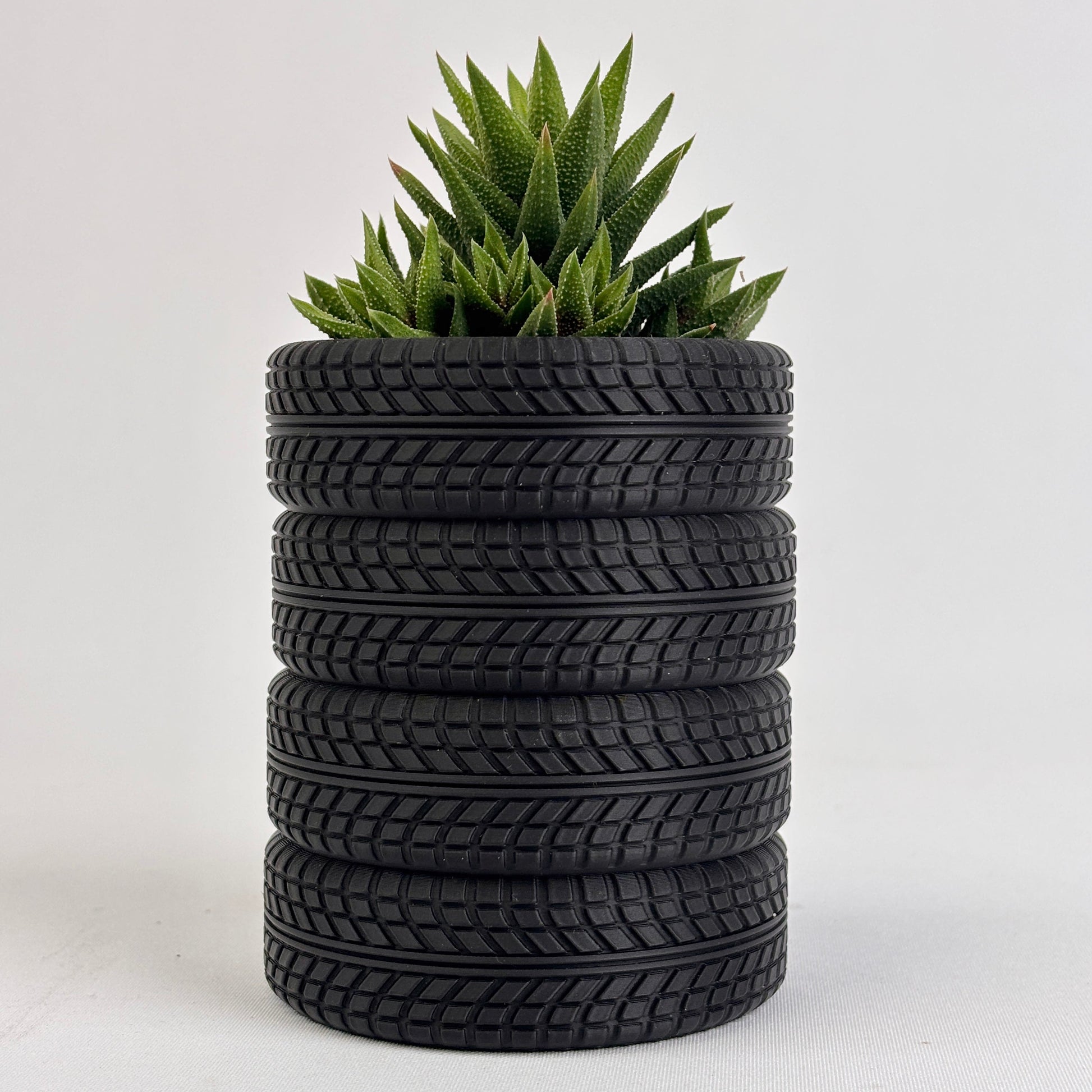 Stack of used tires with a green plant on top against a white background