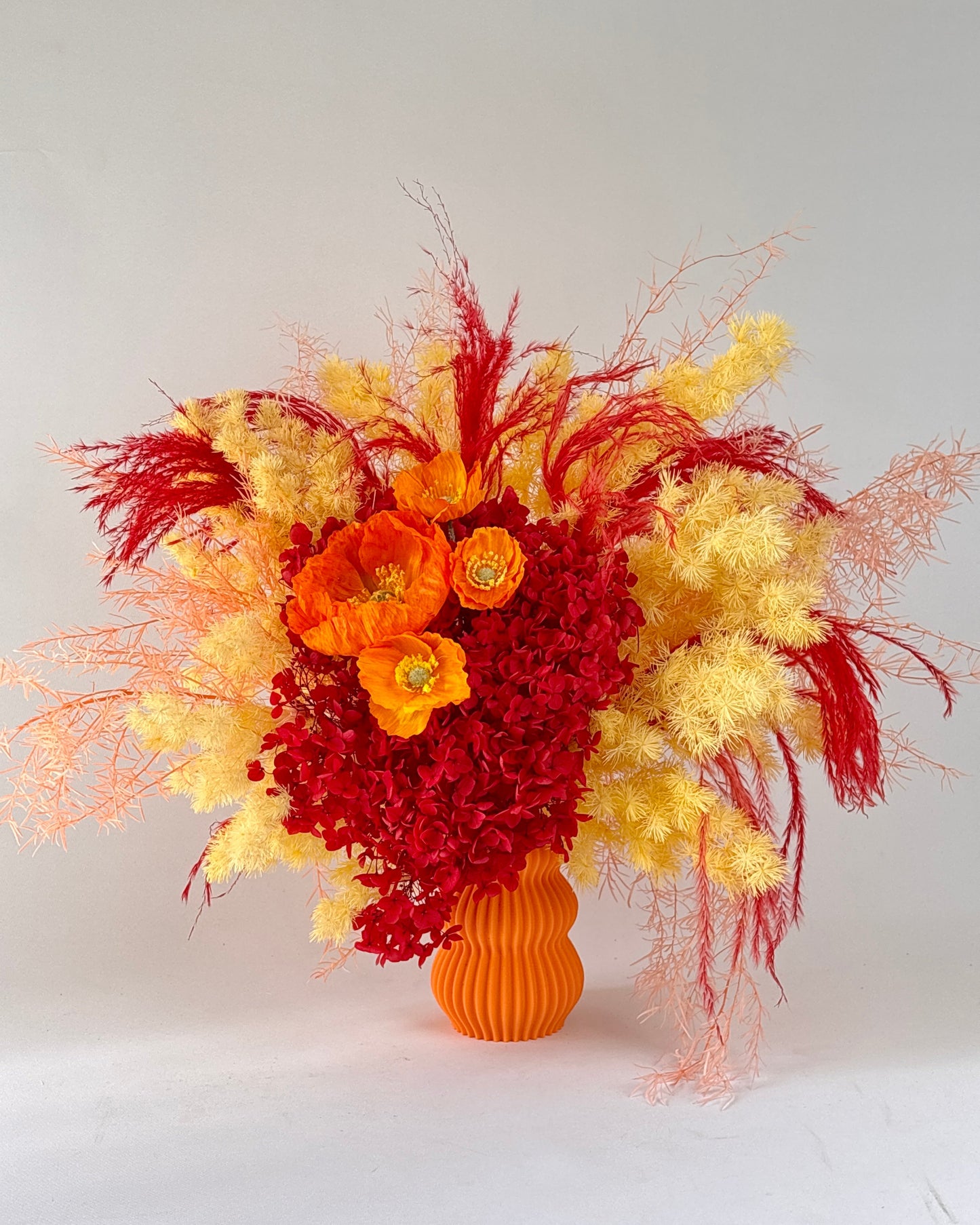 orange yellow dried floral arrangement with red, yellow, and orange flowers in an orange vase on a white background