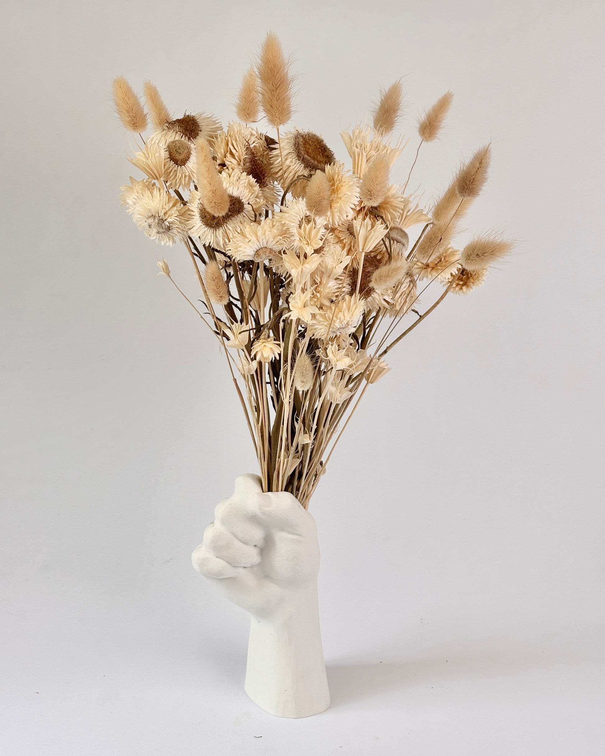 White hand-shaped vase with dried flowers on a light gray background