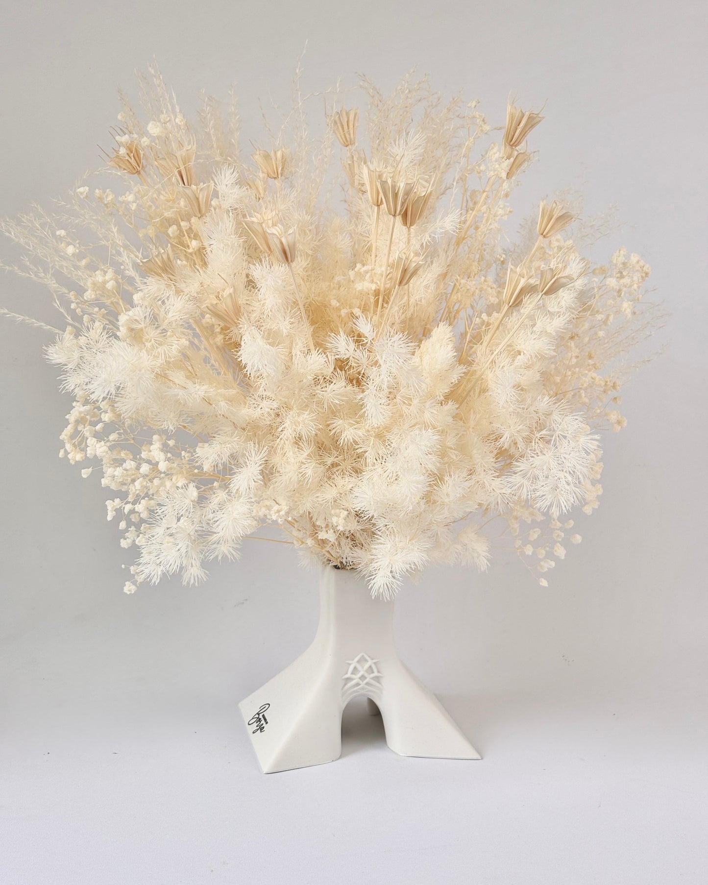White dried flower arrangement in a decorative vase on a light gray background.