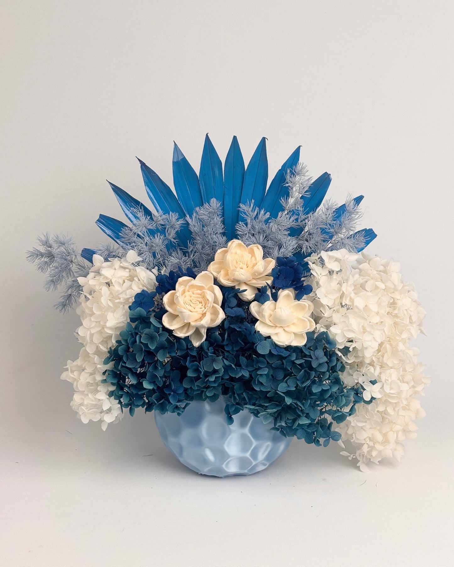 Decorative floral arrangement with blue and white dried flowers in a vase on a light gray background