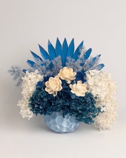 Decorative floral arrangement with blue and white dried flowers in a vase on a light gray background