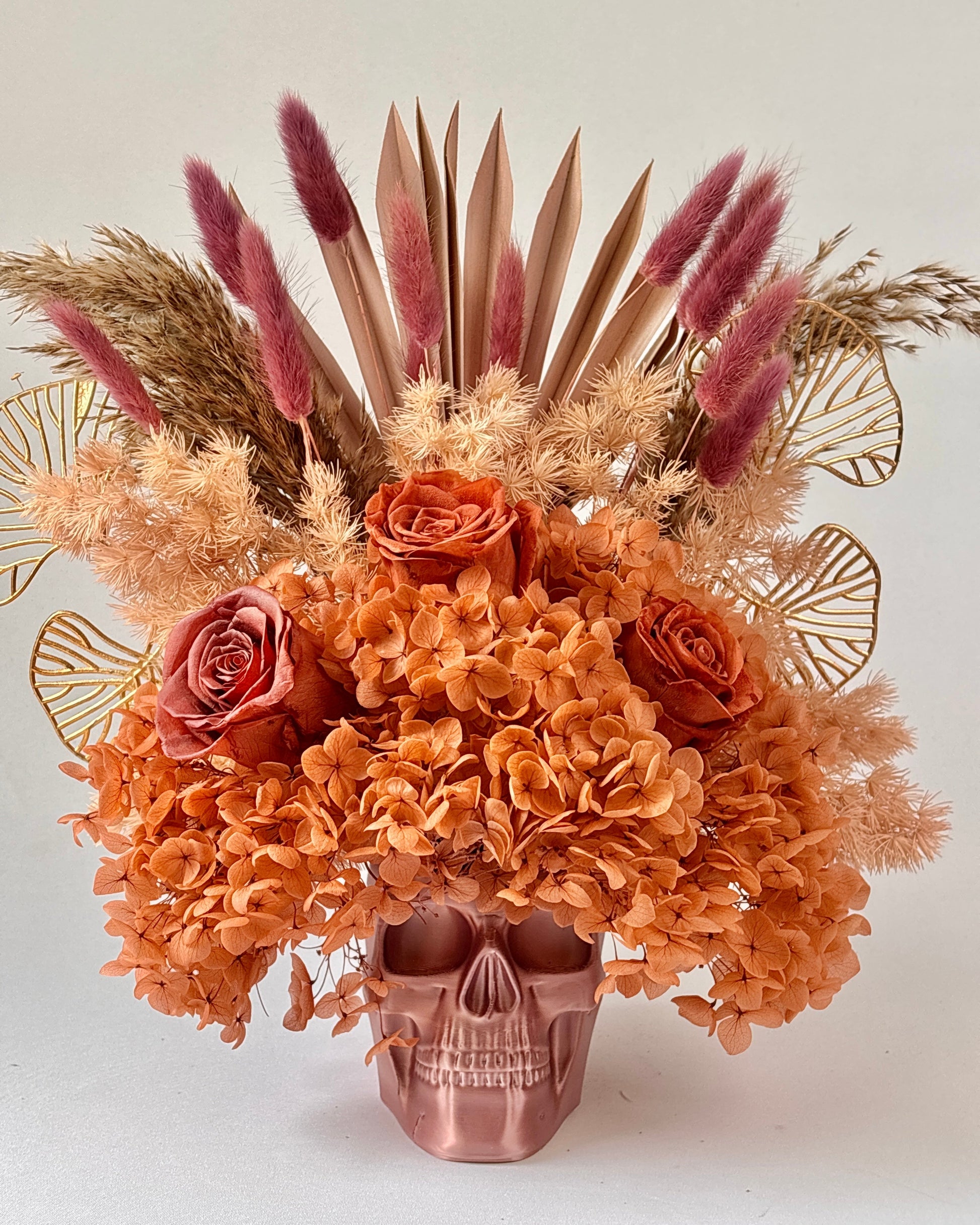 Decorative floral arrangement with dried flowers and a skull-shaped vase on a light background.