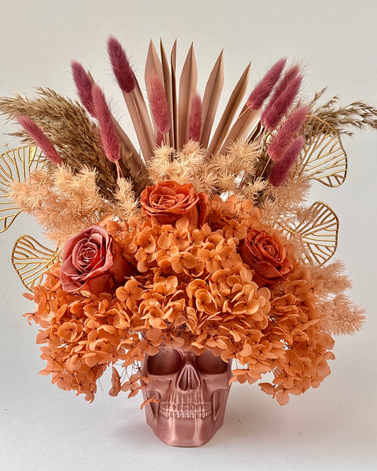 Decorative floral arrangement with dried flowers and a skull-shaped vase on a light background.