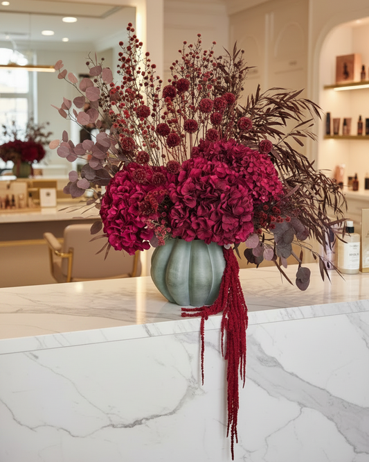 Decorative dried floral arrangement with red flowers and leaves on a marble surface.