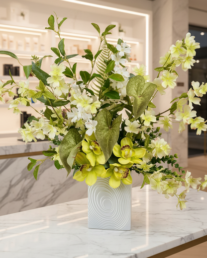 Artificial flower arrangement featuring green orchids, white blossoms, and lush green foliage with ferns and eucalyptus leaves.