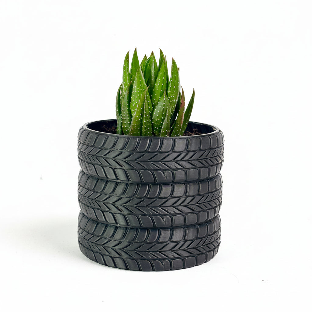 A small green succulent plant in a dark gray planter shaped like stacked car tires, photographed against a plain light background