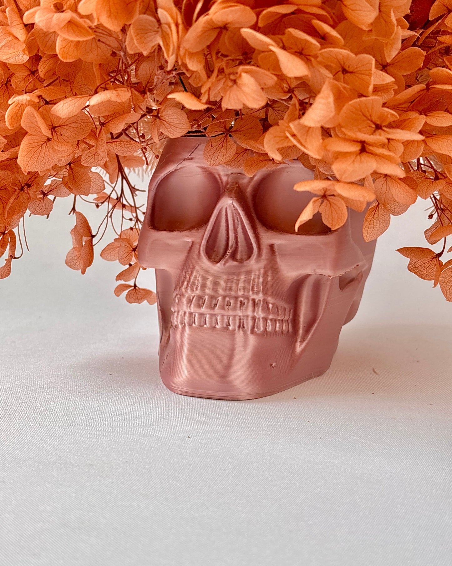 Skull-shaped vase with dried orange flowers on a white background.