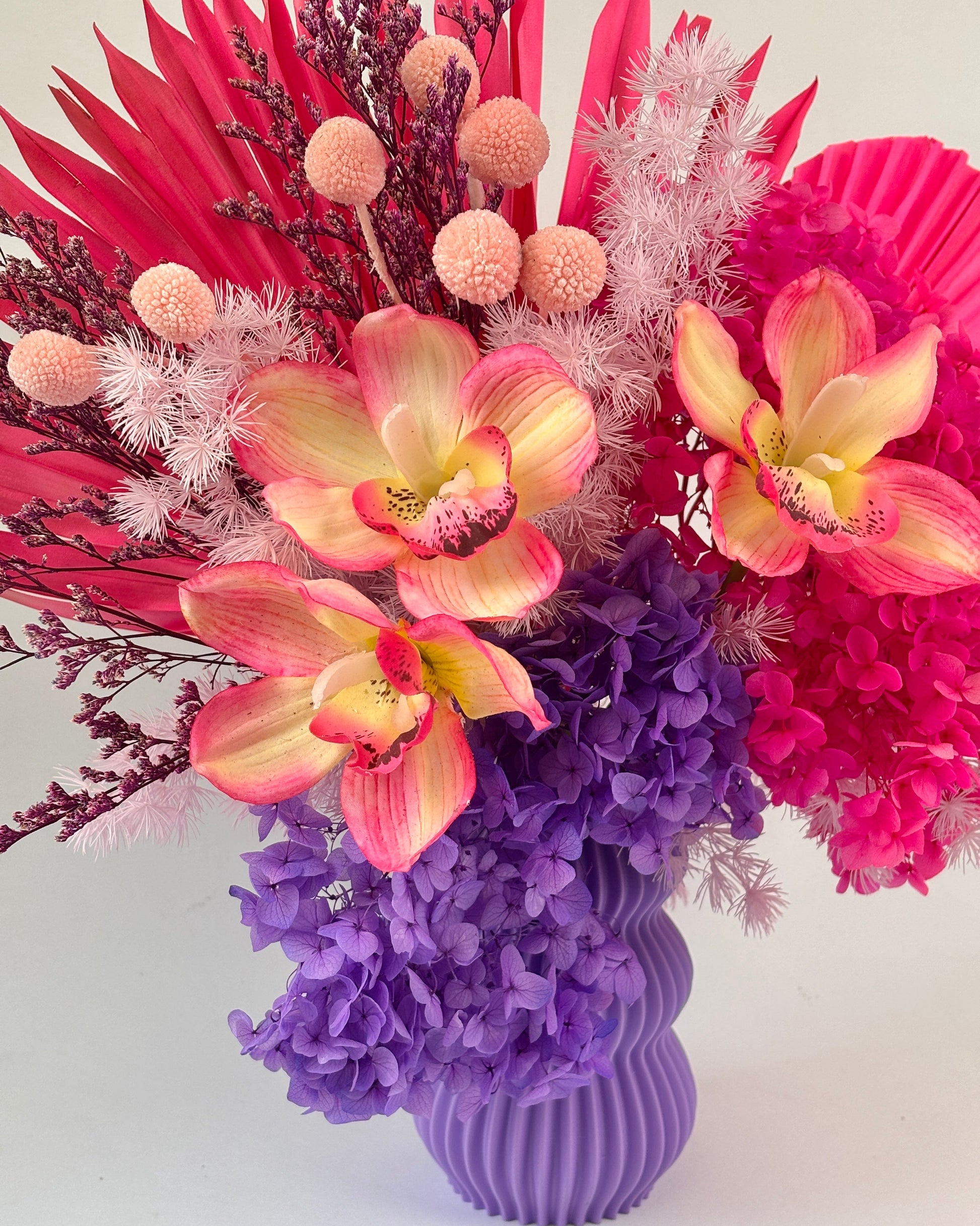 Colourful purple and pink dried flower arrangement with a purple vase on a light background