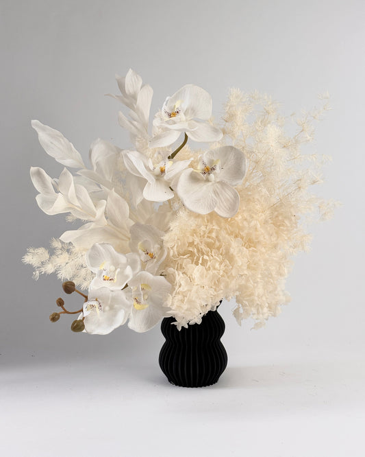 Dried floral arrangement with white and beige flowers in a black vase on a light gray background