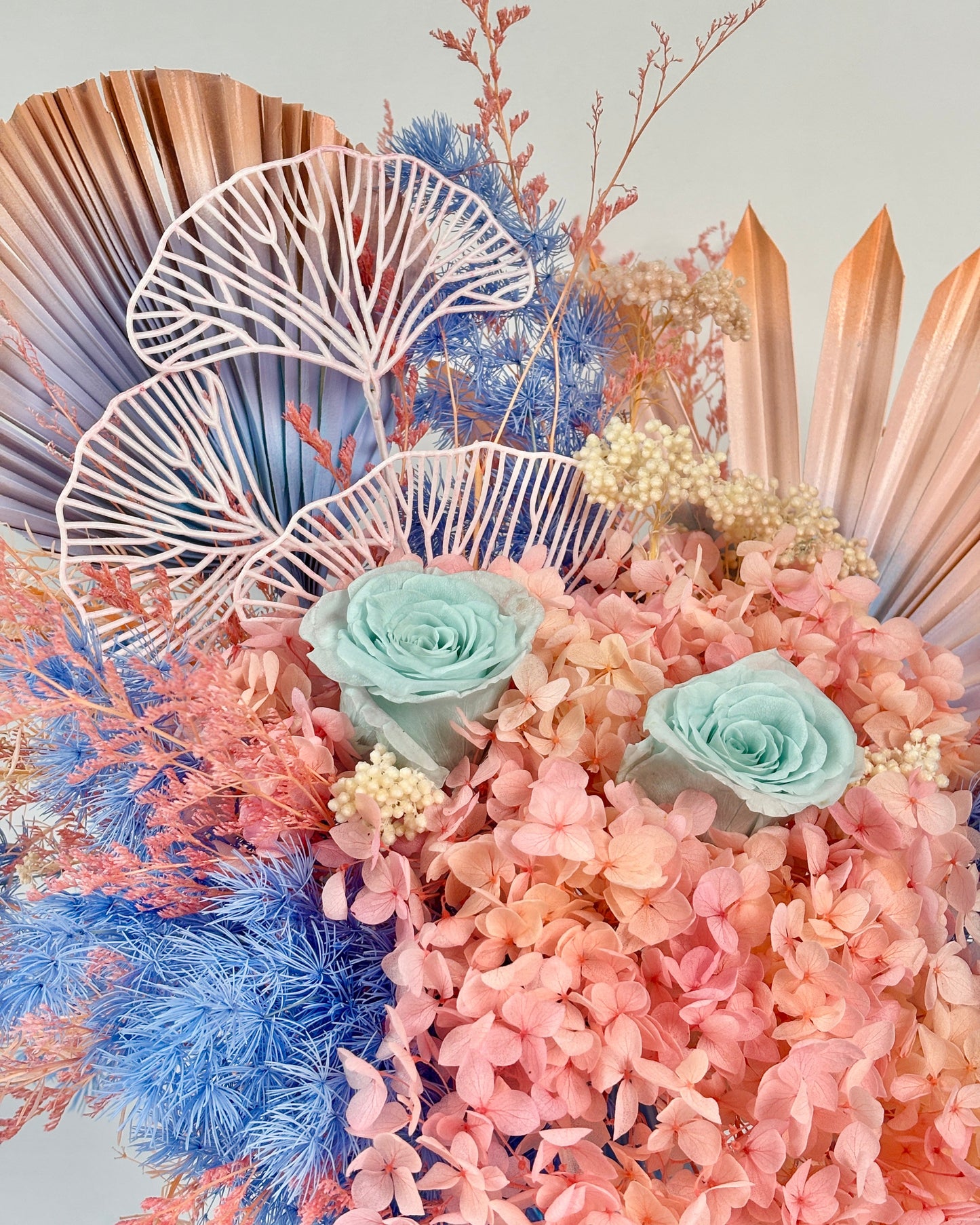 Decorative dried floral arrangement with pink and blue flowers on a light gray background