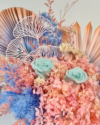 Decorative dried floral arrangement with pink and blue flowers on a light gray background