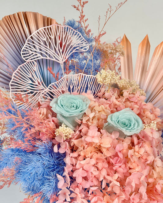 Decorative dried floral arrangement with pink and blue flowers on a light gray background