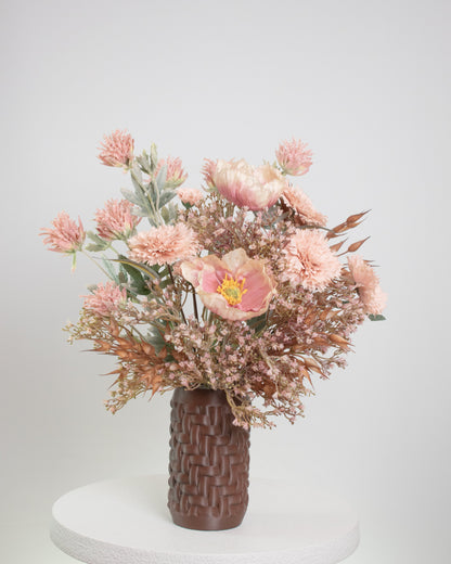 Artificial floral arrangement with blush pink flowers and rustic brown foliage in a woven brown vase, styled on a marble table — a warm, elegant decorative piece perfect for neutral or earthy interiors.