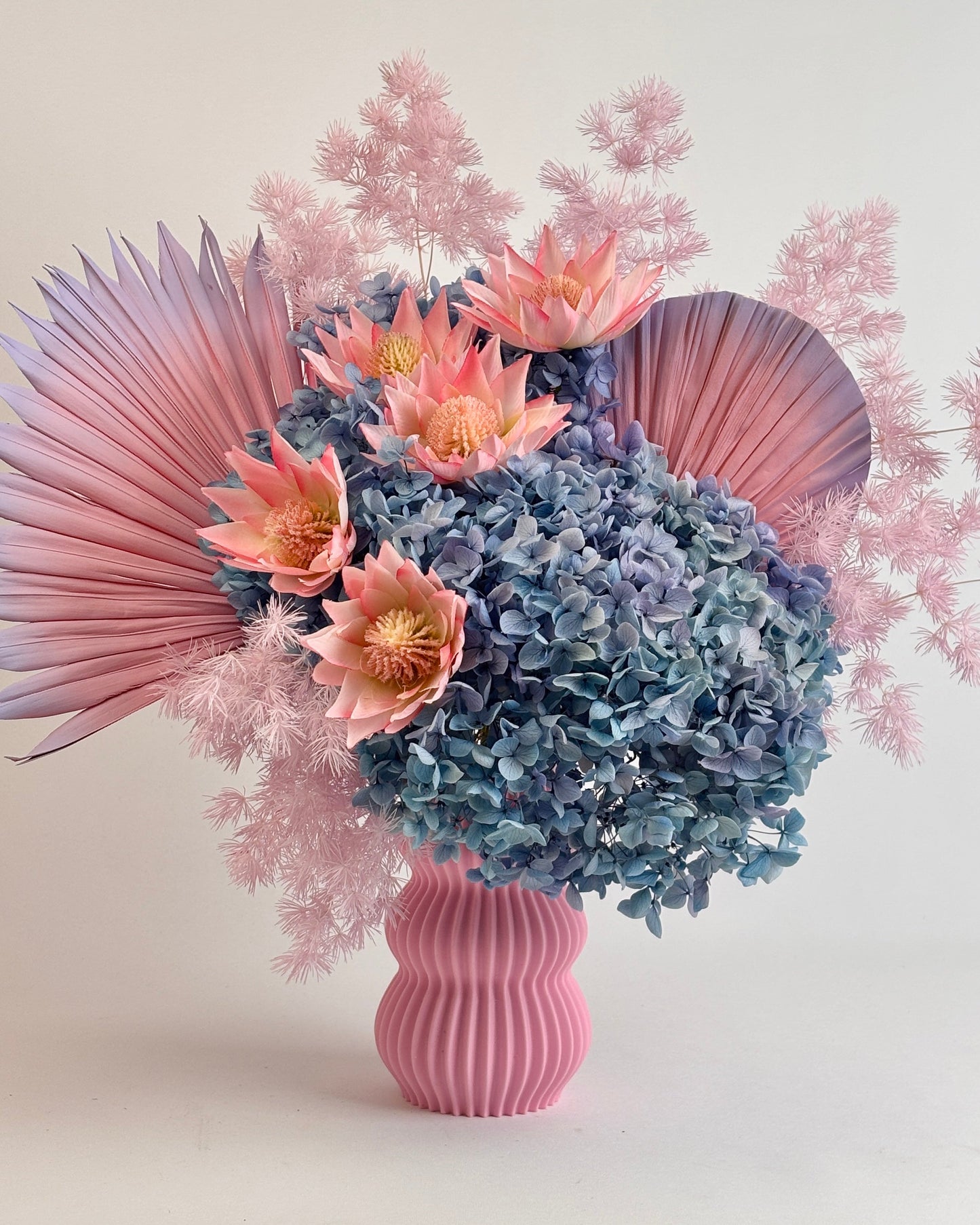 Dried Floral arrangement with pink and blue flowers in a ribbed pink vase on a light background