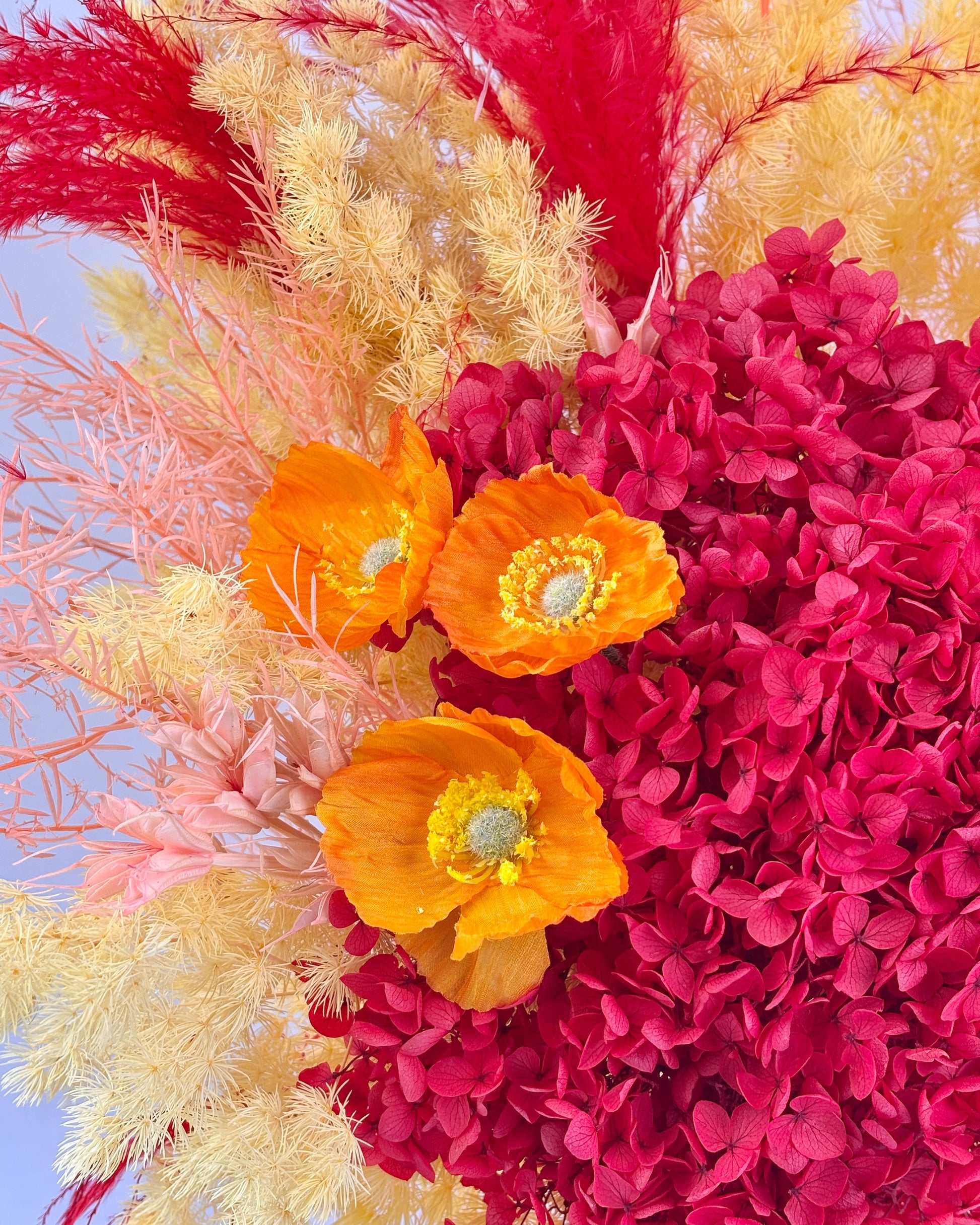 Colorful floral arrangement with orange flowers, pink hydrangeas, and red pampas grass against a blue sky