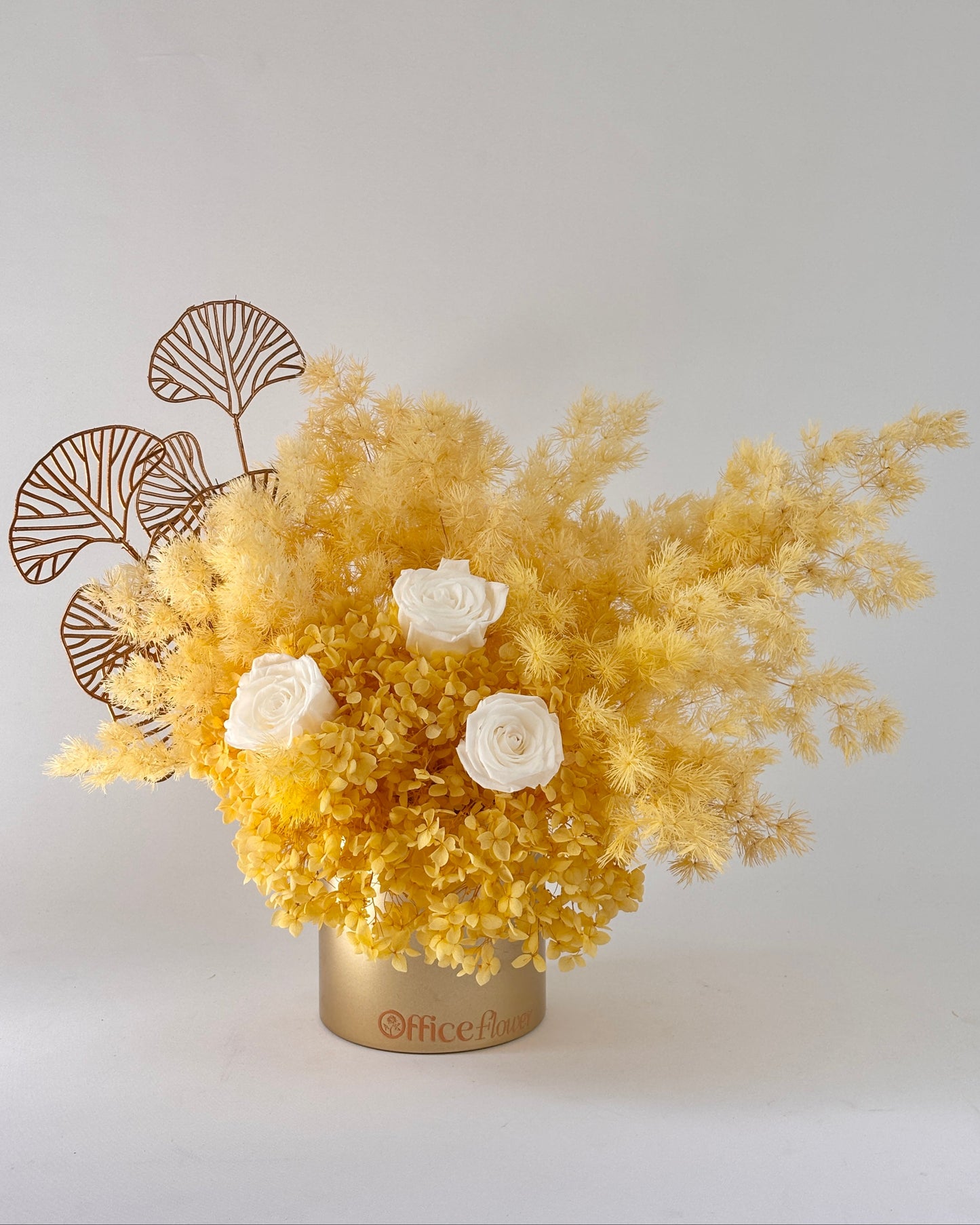 Yellow dried floral arrangement with white roses in a gold vase on a light gray background