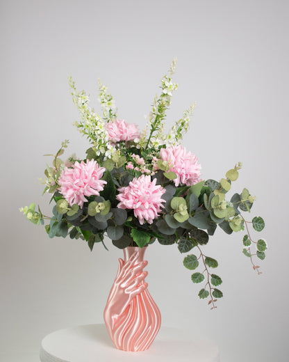 Artificial floral arrangement with pink and white blooms and lush green foliage, elegantly displayed in a sculptural pink hand-shaped vase on a neutral background.