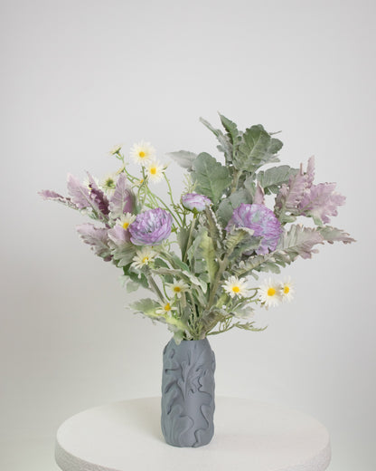 Artificial floral arrangement featuring lavender blooms, white daisies, and green foliage, displayed in a matte grey textured vase on a neutral background.