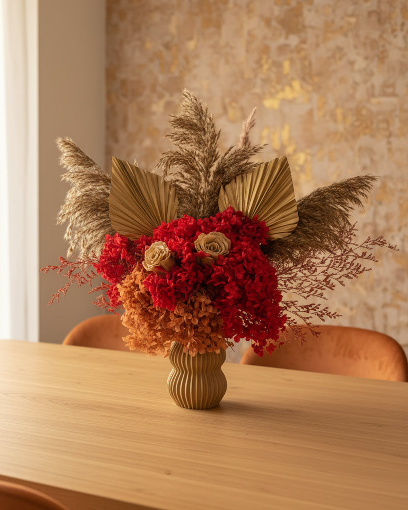 Decorative preserved flowers arrangement with red flowers, gold leaves, and dried grasses on a light gray background